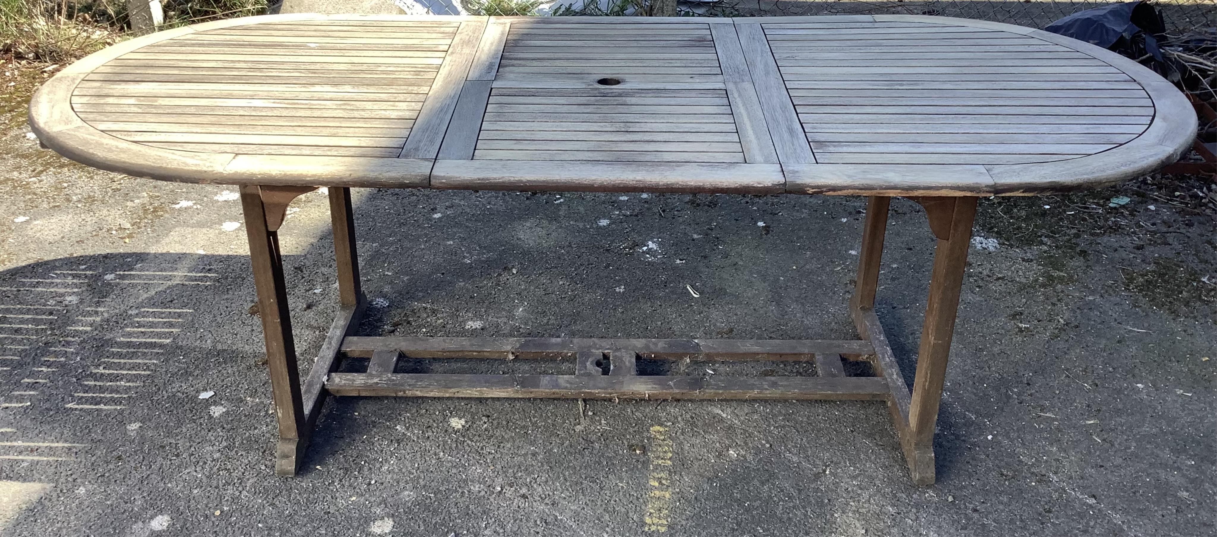 A weathered oval teak extending garden table, width 230cm extended, depth 102cm, height 77cm and six weathered teak folding garden chairs. Condition - fair